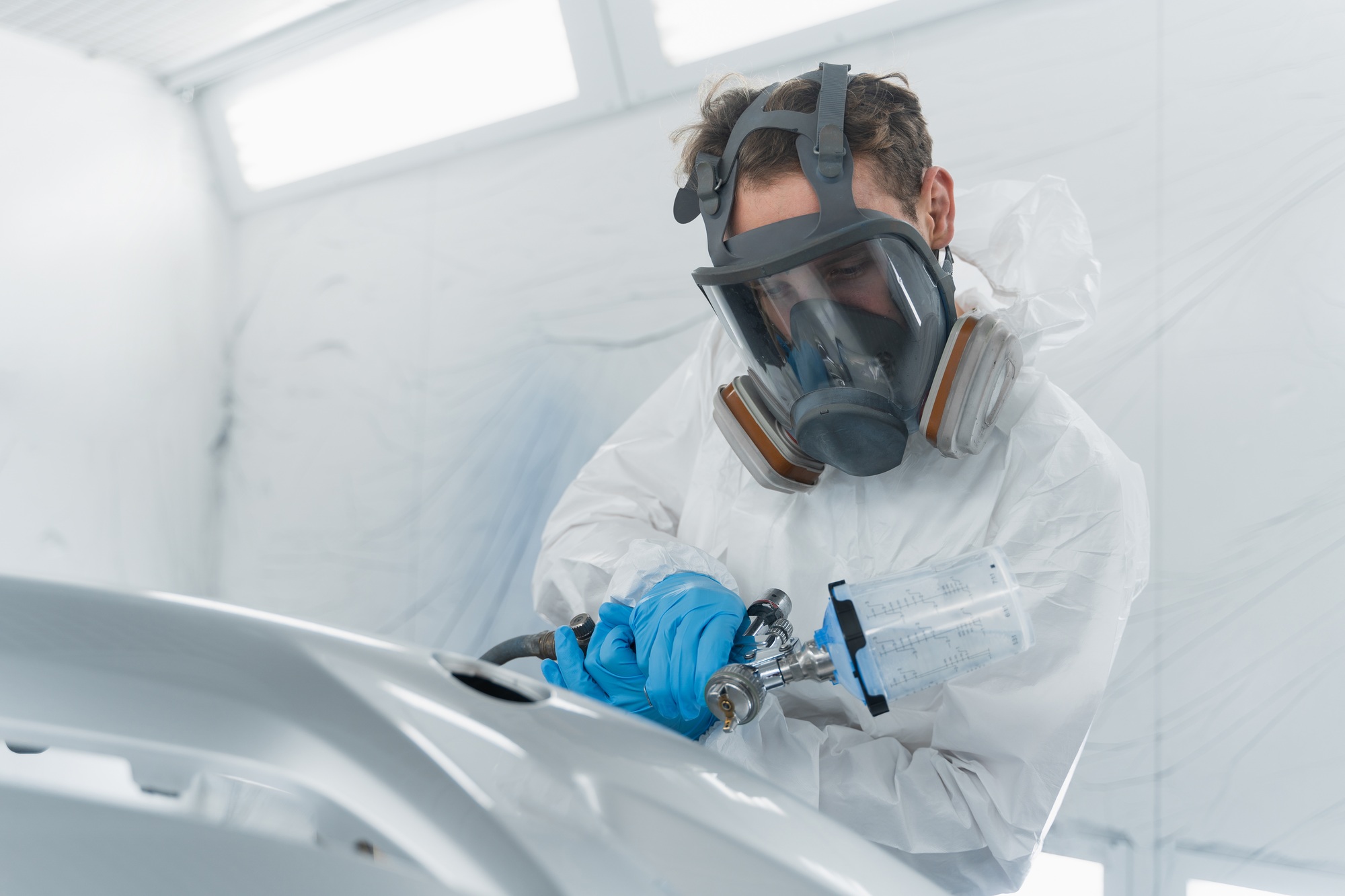 Car painter applies a layer of varnish to the surface of a car bumper.